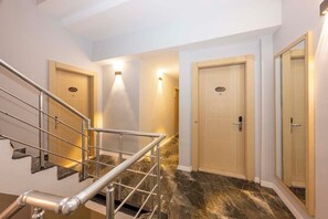 A modern hotel lobby with a marble staircase, a reception desk, and a glass-enclosed elevator.
