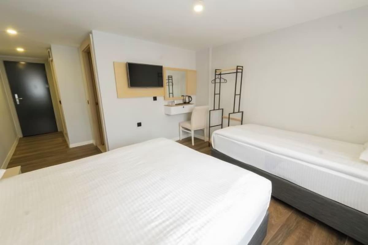 A hotel room with a bed, a desk, a chair, a TV, and a wardrobe.