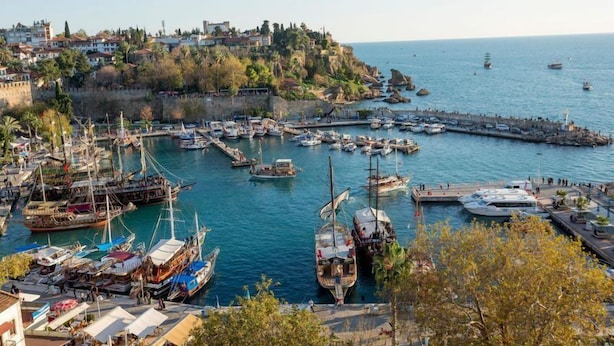 A harbor with boats docked, a pier, and buildings on a hillside. - Legend Tulip Hotel (Antalya)