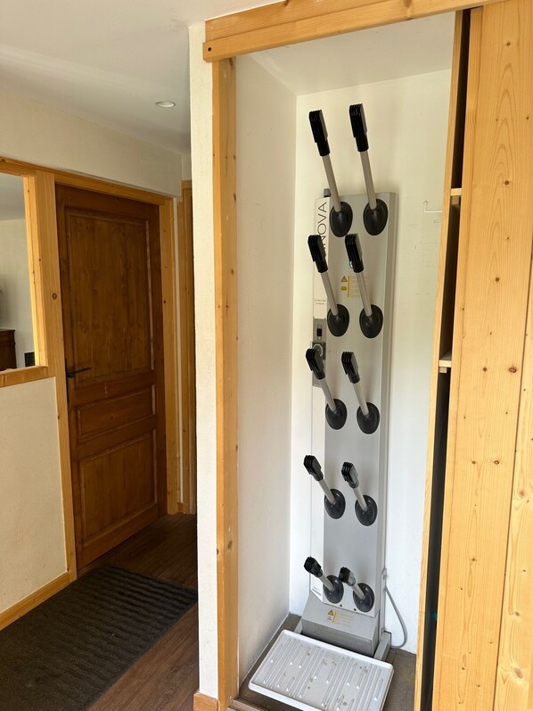 Una habitación con puerta de madera, pared blanca y un perchero metálico con varios ganchos negros.