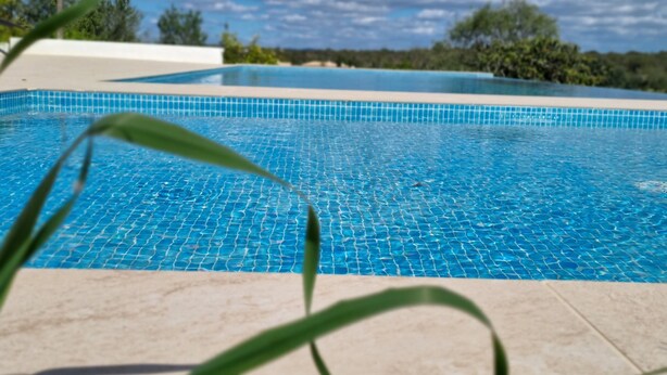 A swimming pool with clear blue water, surrounded by a tiled deck and greenery. - Charming 1-bed House (Silves)