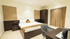 A modern hotel room with a large bed, a desk with a kettle, a chair, and a wardrobe.