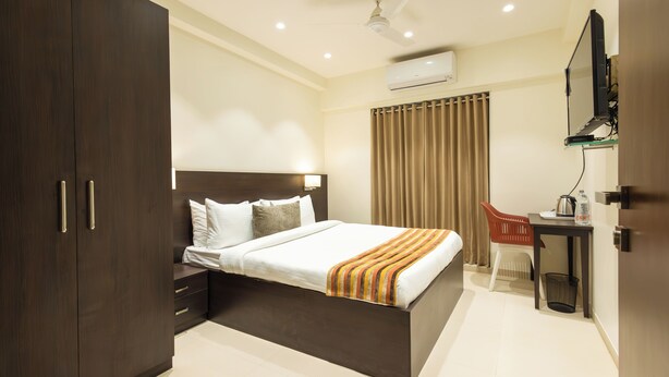 A modern hotel room with a large bed, a desk, a chair, and a wardrobe.