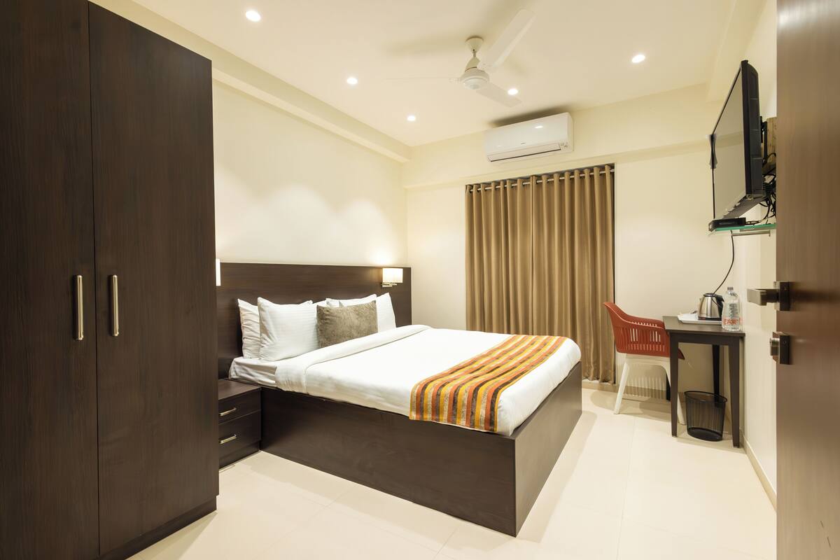 A modern hotel room with a large bed, a desk, a chair, and a wardrobe.