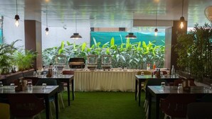 A restaurant with tables and chairs, a green carpet, and hanging lights.