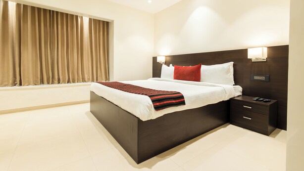 A modern hotel room with a large bed, a nightstand, and a window with curtains.