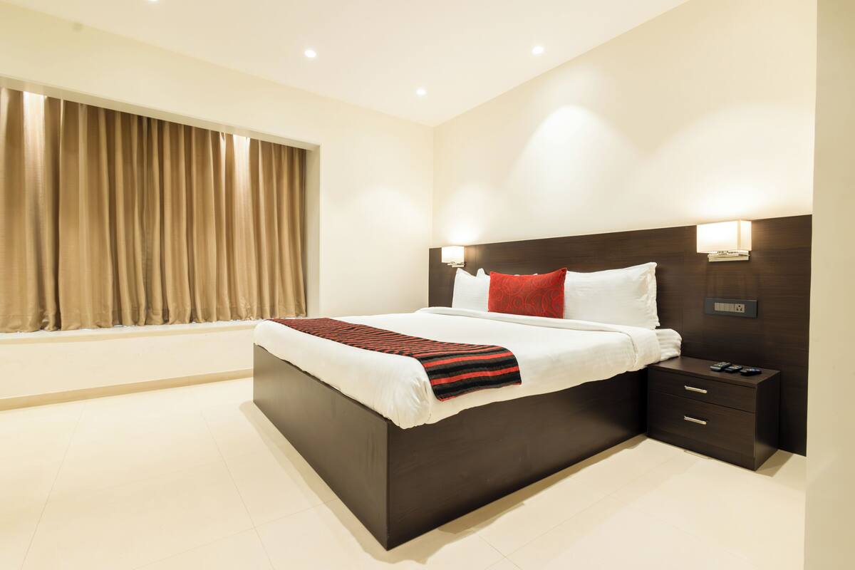 A modern hotel room with a large bed, a nightstand, and a window with curtains.