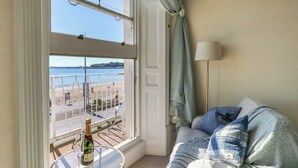Een balkon met een glazen tafel, een fles champagne en uitzicht op het strand.