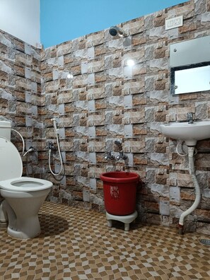 Un baño con pared de piedra, inodoro, calentador de agua rojo y lavamanos.