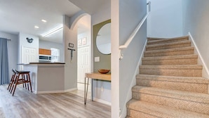 A modern kitchen with a central island, a dining area with a wooden table and chairs, and a staircase with carpeted steps. - 4BR family retreat near Disney w/ patio (Kissimmee)