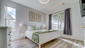 A bedroom with a white bed, green bedding, a bedside table with a lamp, and a window with curtains. - 4BR family retreat near Disney w/ patio (Kissimmee)