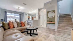 A modern living room with a beige sofa, a round coffee table, and a staircase leading to an upper floor. - 4BR family retreat near Disney w/ patio (Kissimmee)