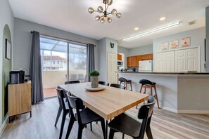 A modern kitchen with white cabinets, a microwave, and a refrigerator. There is a dining area with a wooden table and black chairs. - 4BR family retreat near Disney w/ patio (Kissimmee)