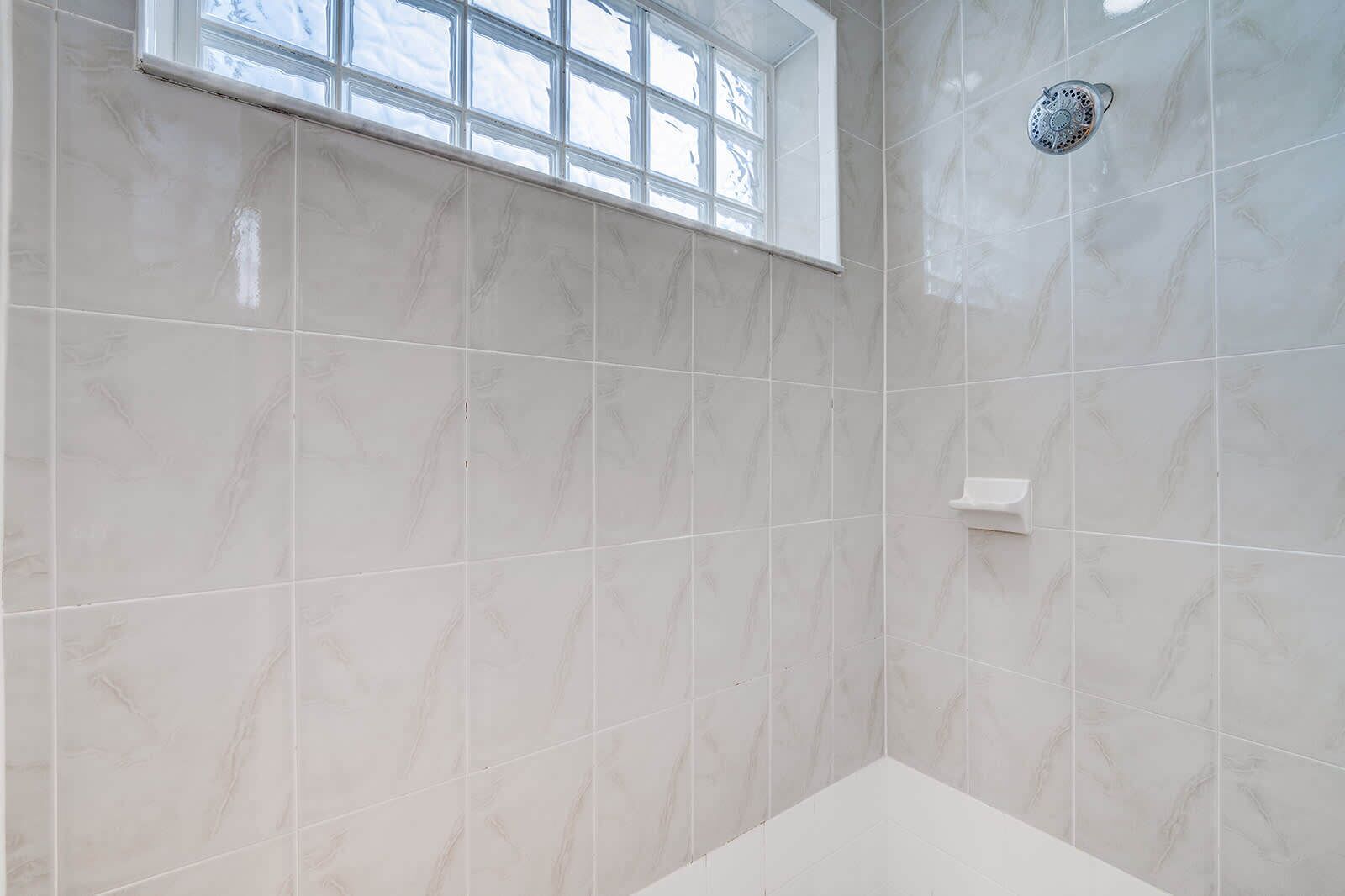 Een badkamer met marmeren tegels, een douche en een raam.