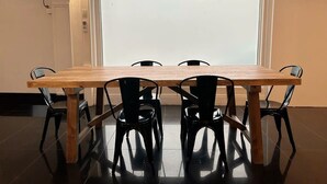 Un coin repas avec une table en bois et des chaises noires, une porte blanche et un luminaire.