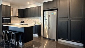 Une cuisine moderne avec des meubles de couleur sombre, un réfrigérateur en acier inoxydable et un îlot central doté de tabourets.