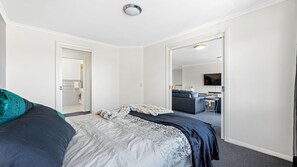 A modern hotel room with a large bed, a separate sitting area with a sofa, a television, and a bathroom visible through an open door. - Unit 9, Boardwalk Apartments (Narooma)