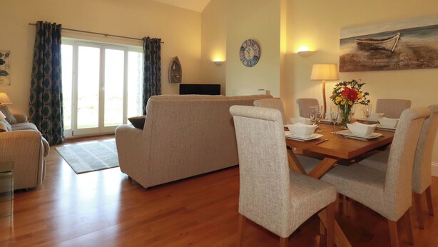 A living room with a sofa, dining table set for four, and a painting on the wall. - Pen-y-les (Wadebridge)