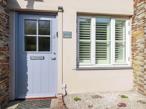A building with a blue door, a window with shutters, and a stone wall. - Pen-y-les (Wadebridge)