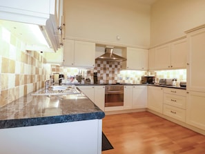 A modern kitchen with a granite countertop, stainless steel appliances, and a checkered backsplash. - Pen-y-les (Wadebridge)