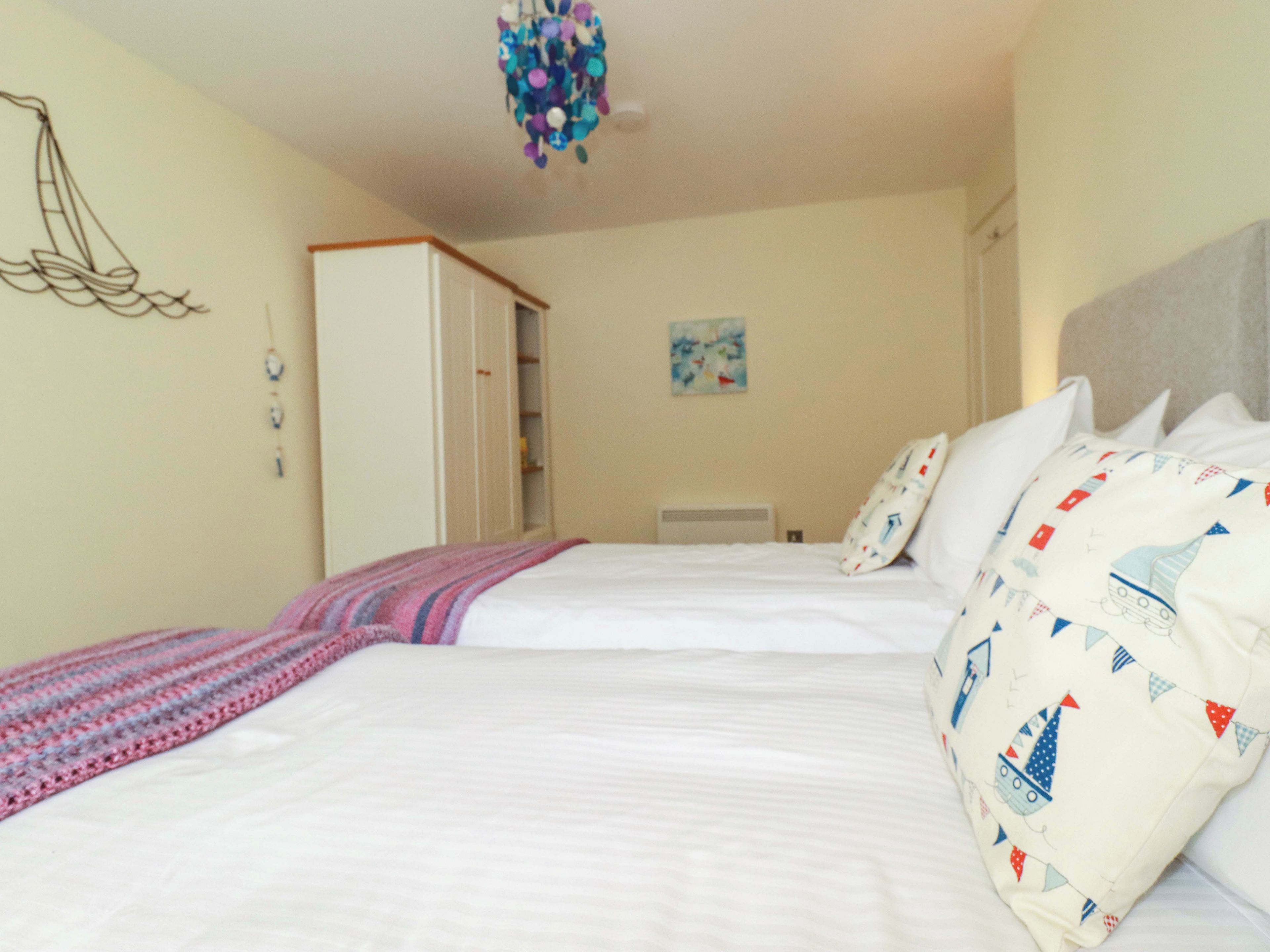 A bedroom with two beds, a wardrobe, a painting on the wall, and a ceiling light fixture.