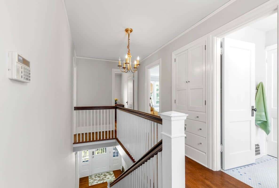 Una escalera con barandillas blancas y un candelabro, que conduce a una habitación con puertas blancas y una toalla verde colgada de una puerta.