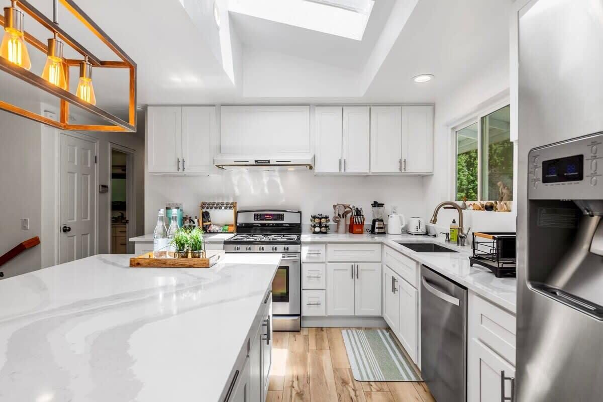 A modern kitchen with white cabinetry, a central island, stainless steel appliances, and a skylight.