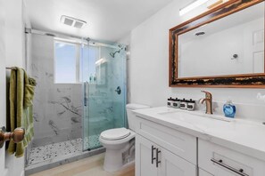 Ein modernes Badezimmer mit einer gläsernen Duschkabine, einer weißen Toilette und einem Waschtisch mit großem Spiegel.