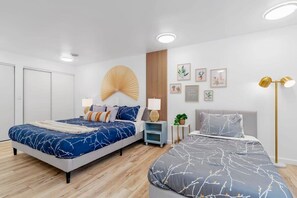 Ein modernes Schlafzimmer mit zwei Betten, einem großen Ventilator, Nachttischen und Wandbildern.