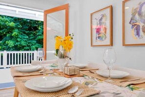 A dining table set with white plates, cutlery, and glasses, with a vase of yellow flowers and framed artwork on the wall.