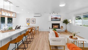 A modern kitchen with a bar area, a fireplace, and a dining space with a white sofa and orange chairs. - Bothell Family Friendly Modern Home, 2 AC, I405 (Bothell)