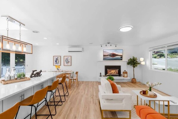 Eine moderne Küche mit Barbereich, Kamin und Essbereich mit weißem Sofa und orangefarbenen Stühlen.