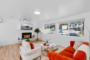 A modern living room with a fireplace, white sofas, a bright window, and a view of the outside.