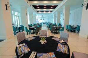 Enjoy meals in this stylish dining area with a round table, teal chairs, and elegant table settings.