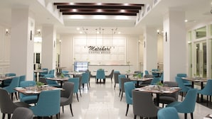 Uma área de refeições moderna com várias mesas e cadeiras, um espaço central para café e uma placa com a inscrição "Madhari Coffee House".