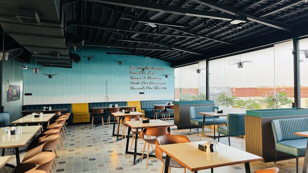 A restaurant interior with booths and tables, a blue wall with text, and large windows. - Hotel Tirth by Sonu Cafe (Ujjain)