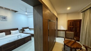 A hotel room with a large bed, a wooden wardrobe, a small table, and a chair. - Hotel Tirth by Sonu Cafe (Ujjain)