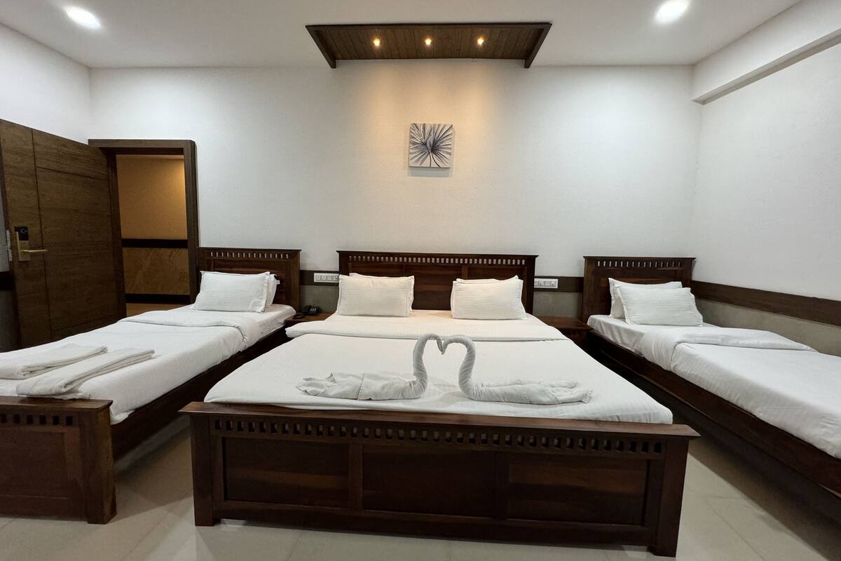 A hotel room with three single beds, a wooden wardrobe, and a ceiling light fixture.