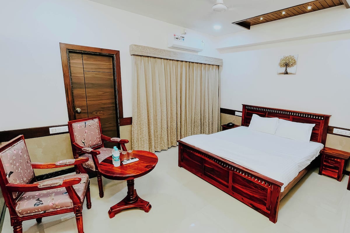 A hotel room with a wooden bed, a small table with a chair, a desk, and a wardrobe.