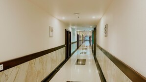 A long, well-lit hallway with marble flooring, doors, and light fixtures. - Hotel Tirth by Sonu Cafe (Ujjain)