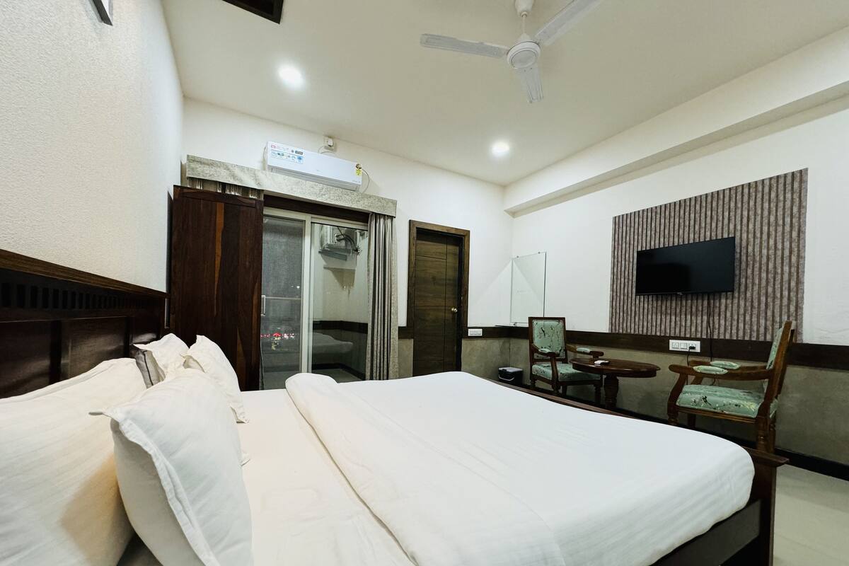 A hotel room with a large bed, a ceiling fan, a flat-screen TV mounted on the wall, and a sliding glass door leading to a balcony.