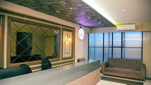 A reception area with a glass counter, a sofa, and a large window with curtains. - Hotel Tirth by Sonu Cafe (Ujjain)