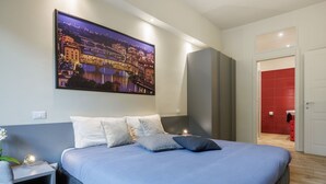 Ein modernes Hotelzimmer mit einem großen Bett, einem Nachttisch, einem an der Wand befestigten Fernseher und einem roten Badezimmer, das durch eine offene Tür sichtbar ist.