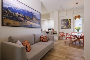 A modern living room with a sofa, a dining area with red chairs, and a kitchen in the background.