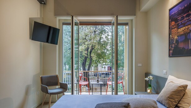 Ein Schlafzimmer mit einem Bett, Kissen, einem Fernseher, einem Sessel und einem Balkon mit Tisch und Stühlen.