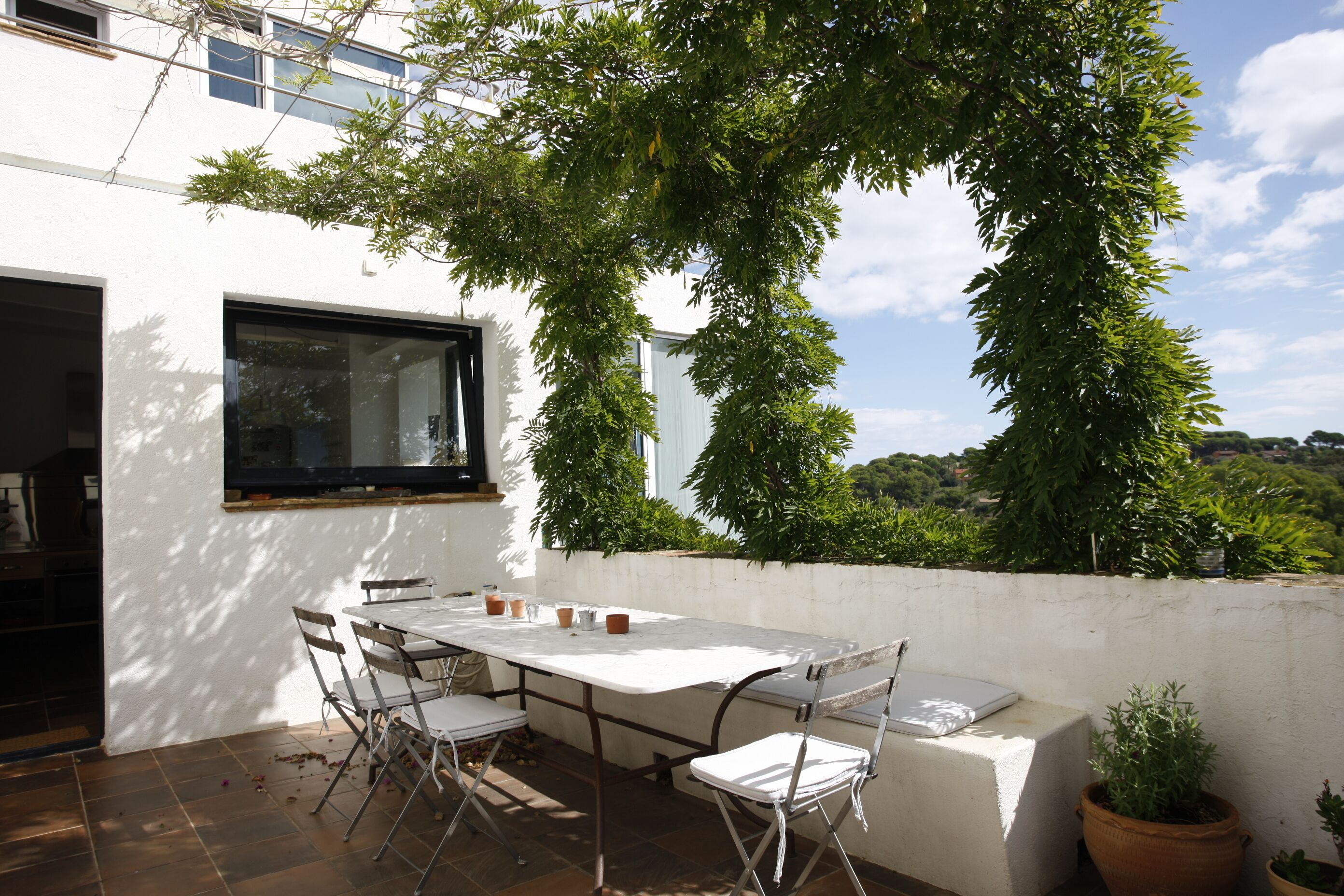 Un patio con una mesa, sillas, una computadora portátil y plantas en macetas.
