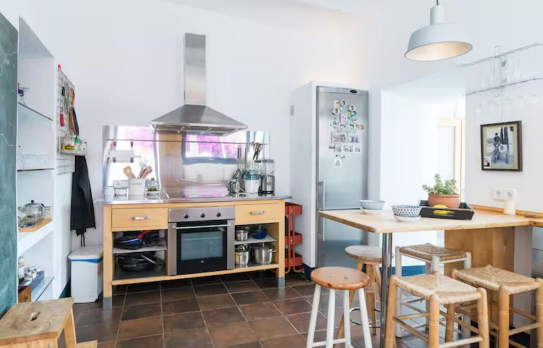 A compact kitchen with a stove, oven, and refrigerator, a dining area with stools, and a hanging light fixture.