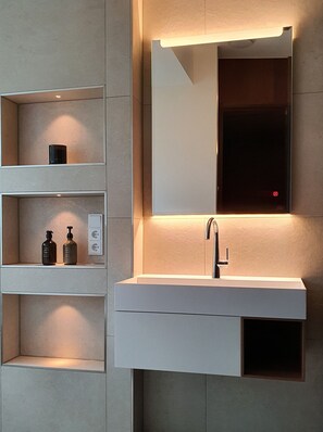 A modern bathroom with a built-in sink, a mirror, and shelves with toiletries. - Villa Baltique Sellin (Sellin)