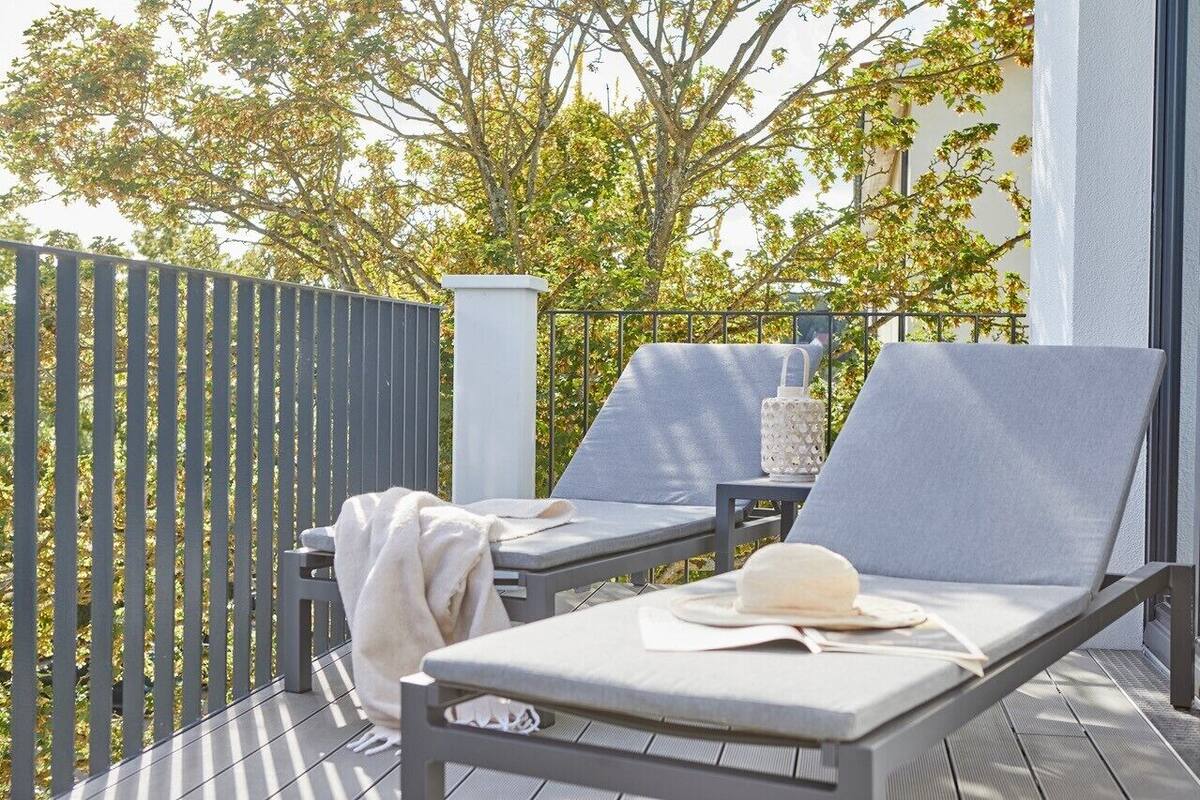 Een balkon met twee grijze loungesteunen, een witte vaas en een hoed op één van de stoelen.