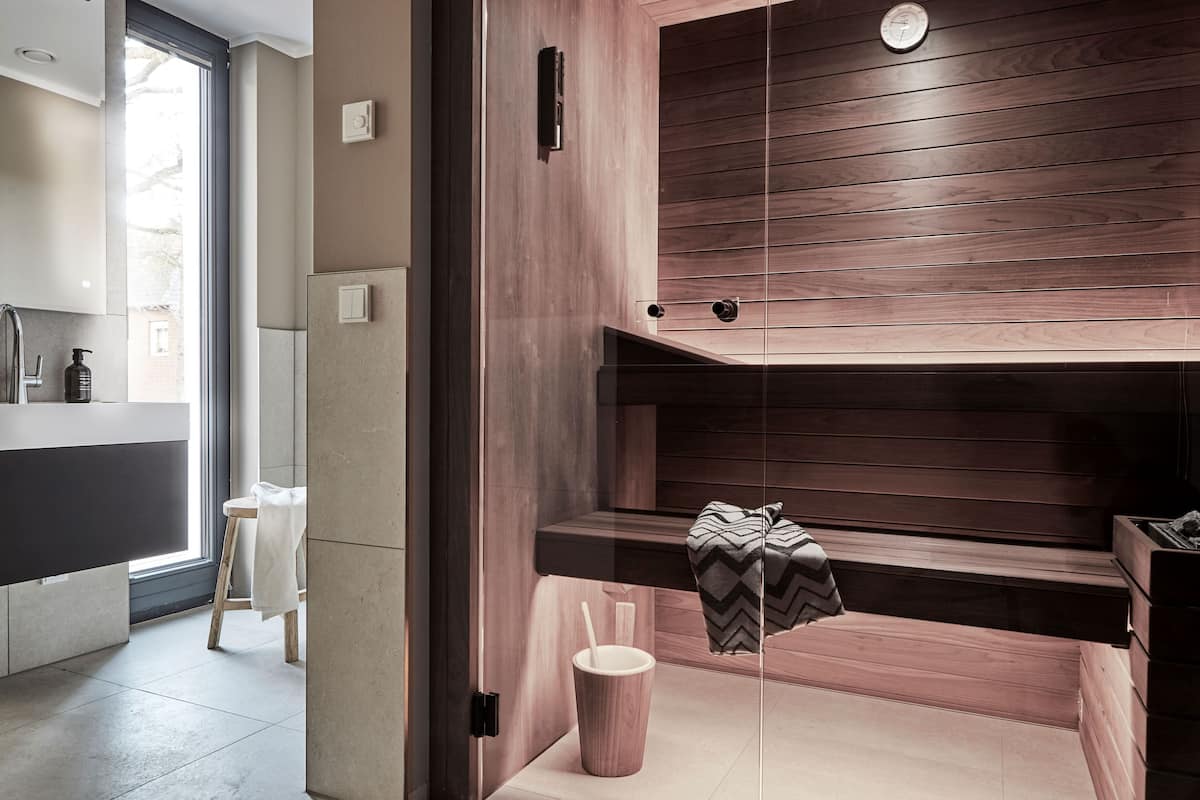 Een moderne badkamer met een houten wastafel, een bankje en een klein tafeltje met een handdoek en een beker.